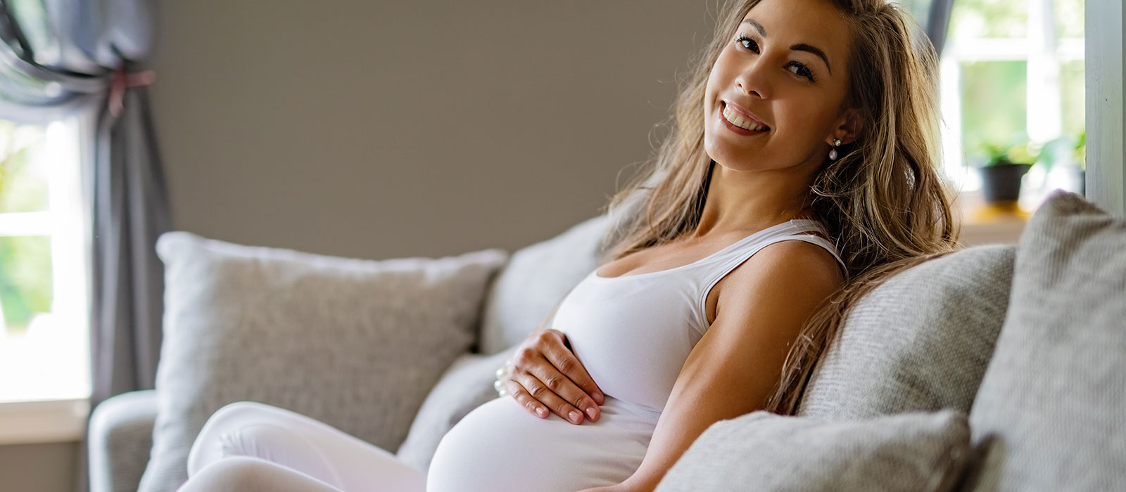 happy pregnant woman sitting in sofa touching her belly