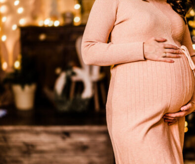 Woman in front of holiday lights celebrating her pregnancy during the holidays