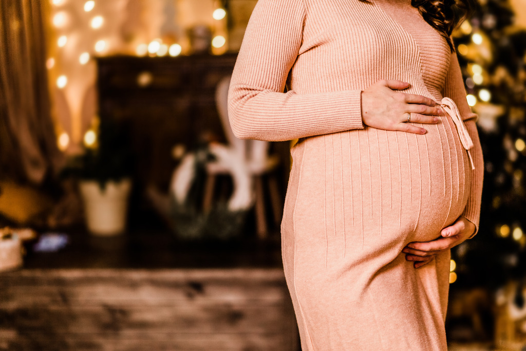 Woman in front of holiday lights celebrating her pregnancy during the holidays