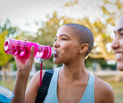 A Young African American Woman Drinking Water from a Pink Water Bottle Outside How To Prevent a UT