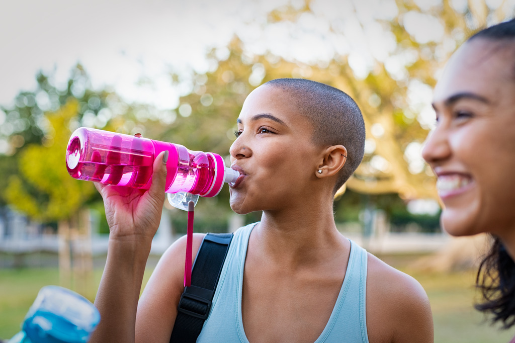 A Young African American Woman Drinking Water from a Pink Water Bottle Outside How To Prevent a UT