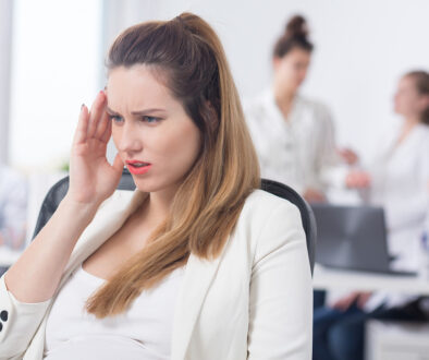 Professionally Dressed Woman Holding Her Head While Sitting in an Office Dealing with Signs of Pregnancy Before Missed Period