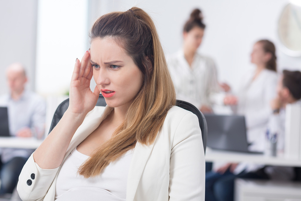 Professionally Dressed Woman Holding Her Head While Sitting in an Office Dealing with Signs of Pregnancy Before Missed Period