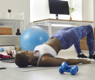 An African American Woman Doing a Bridge Exercise on a Yoga Mat at Home While Watching a Workout Video Pelvic Floor Muscles