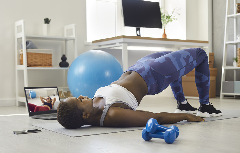 An African American Woman Doing a Bridge Exercise on a Yoga Mat at Home While Watching a Workout Video Pelvic Floor Muscles