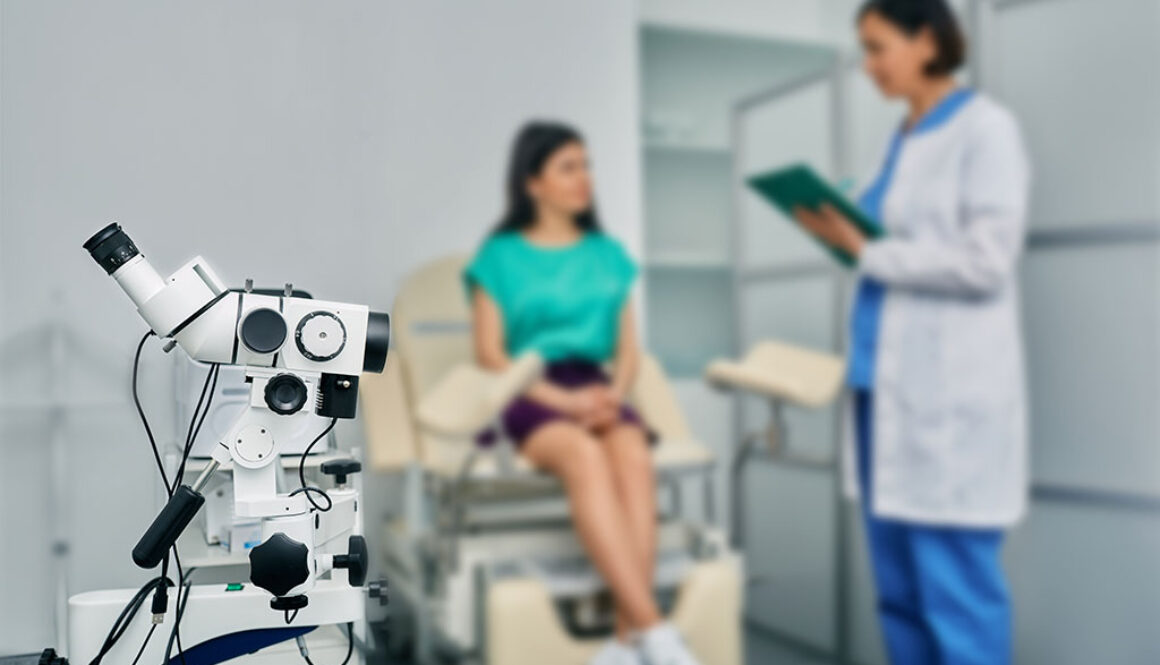 Closeup of a Colposcopy Machine With a Gynecologist Speaking to a Young Woman Patient in the Background