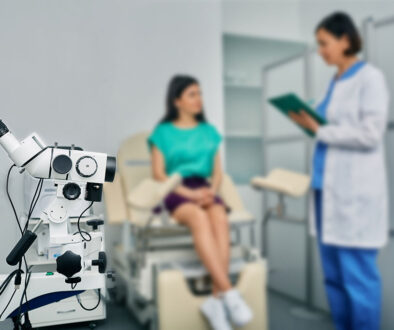 Closeup of a Colposcopy Machine With a Gynecologist Speaking to a Young Woman Patient in the Background