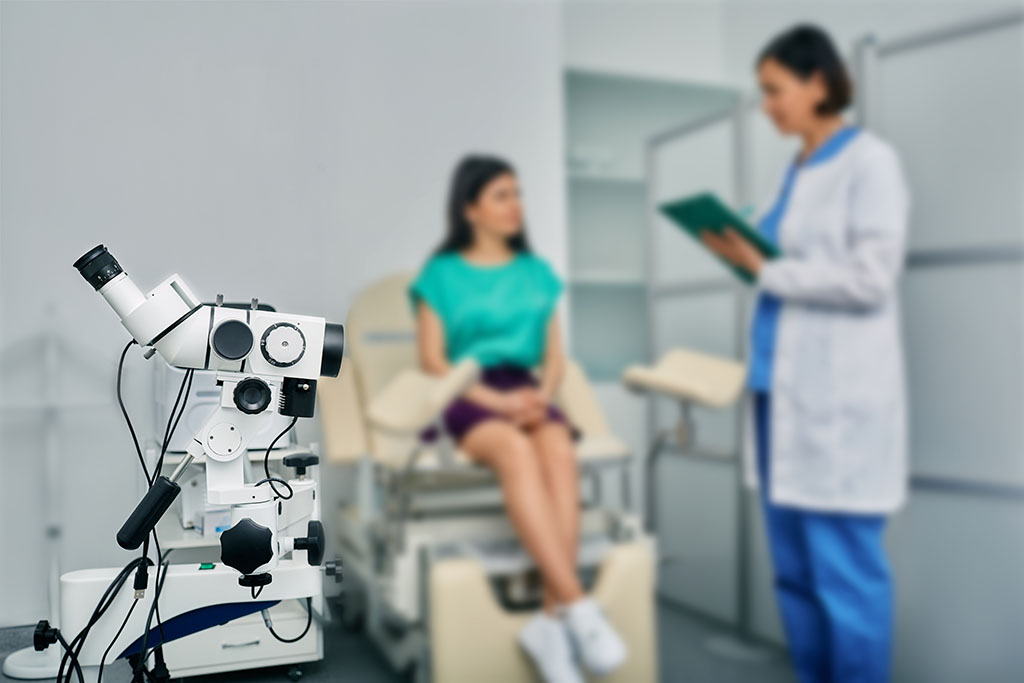 Closeup of a Colposcopy Machine With a Gynecologist Speaking to a Young Woman Patient in the Background