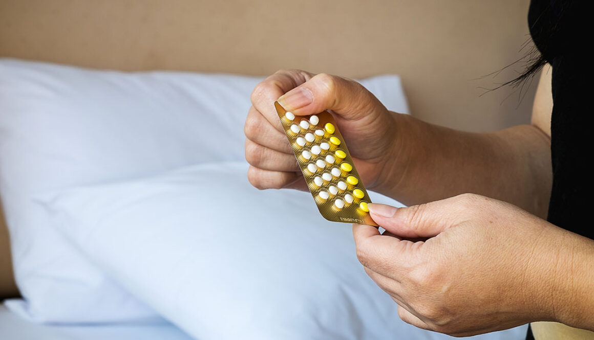Closeup of a Woman Holding Birth Control Pills With a Bed in the Background Does Birth Control Affect Sex Drive