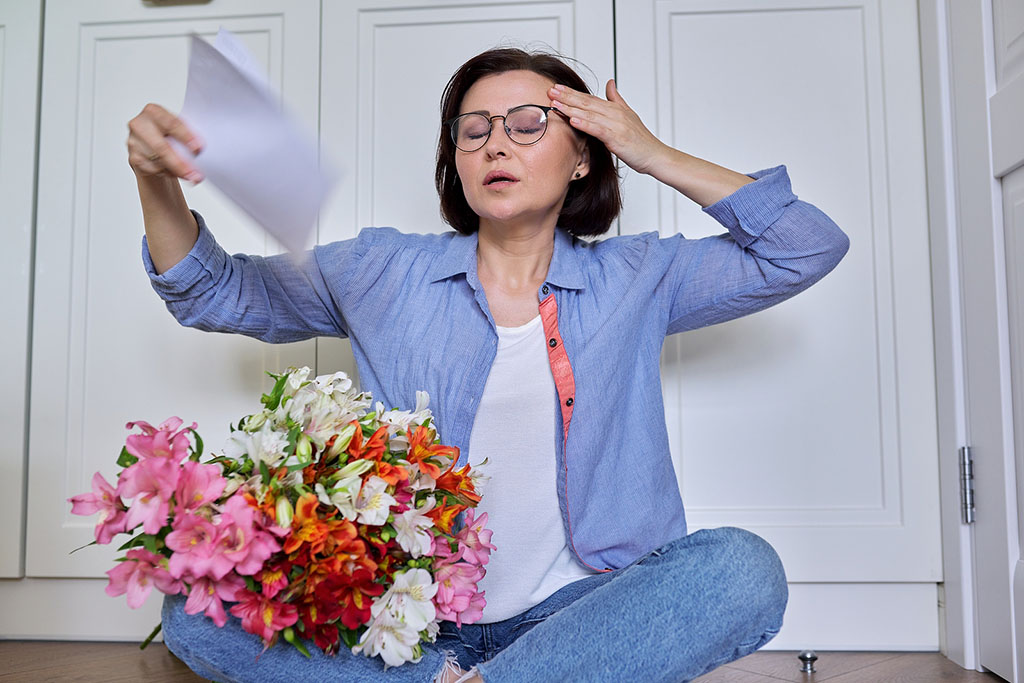 A Middle-Aged Woman Sitting On The Floor Fanning Herself With Sheets Of Paper Signs Perimenopause Is Ending